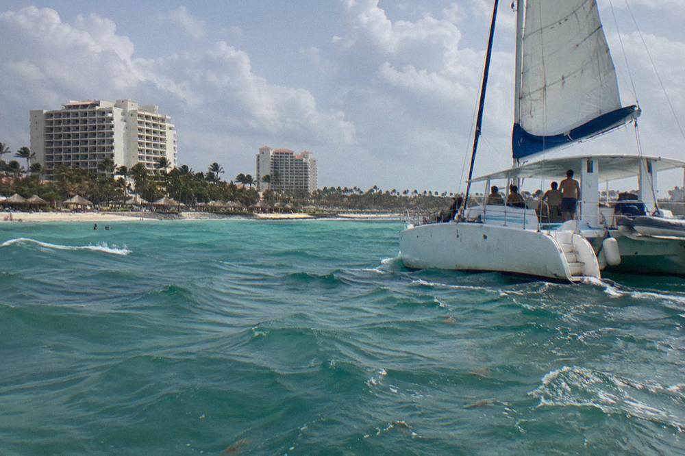 Open deck catamaran with sails up cruising the calm water off Palm Beach before sunset